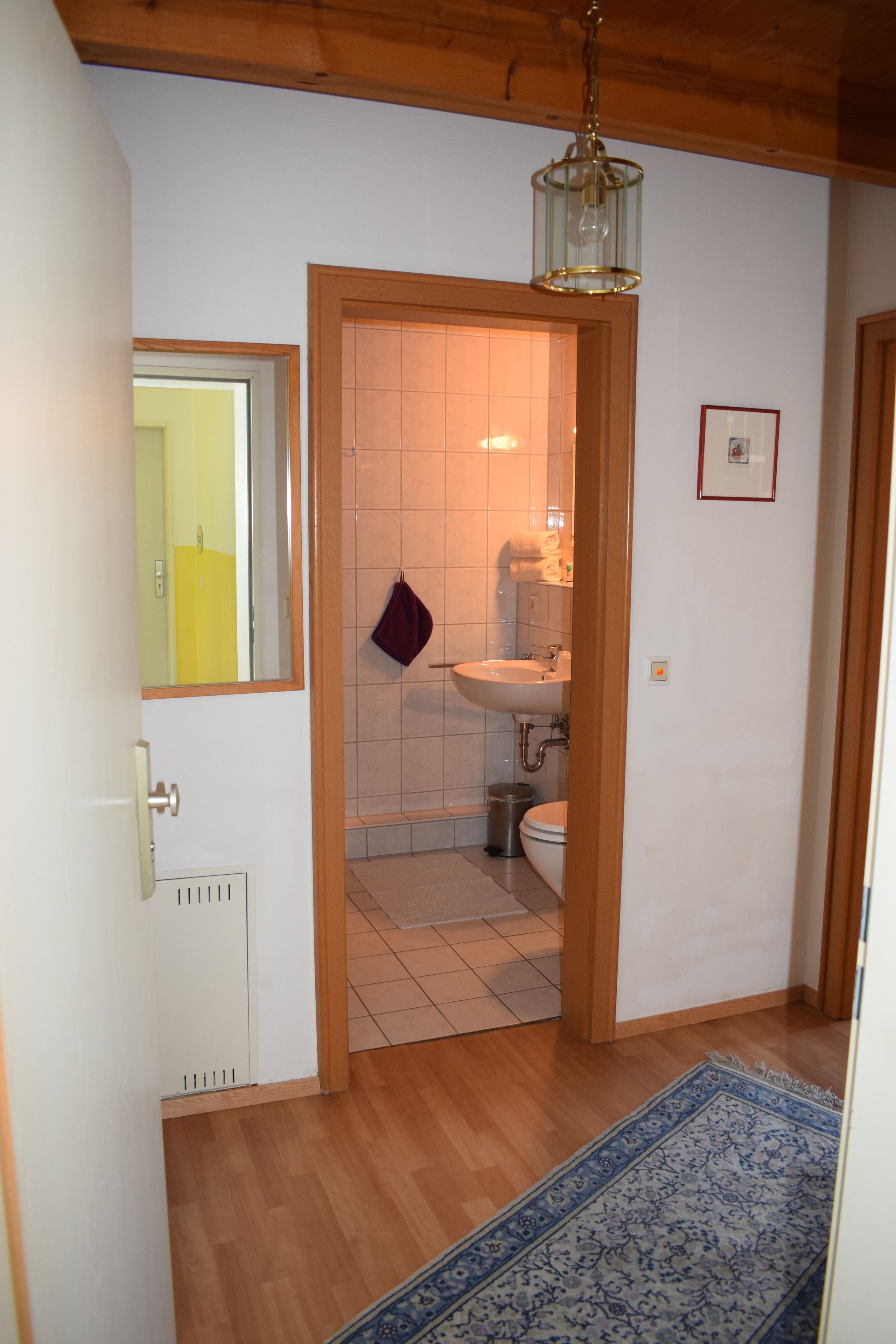 A hallway leading to a bathroom with a tiled floor, a sink, and a toilet.