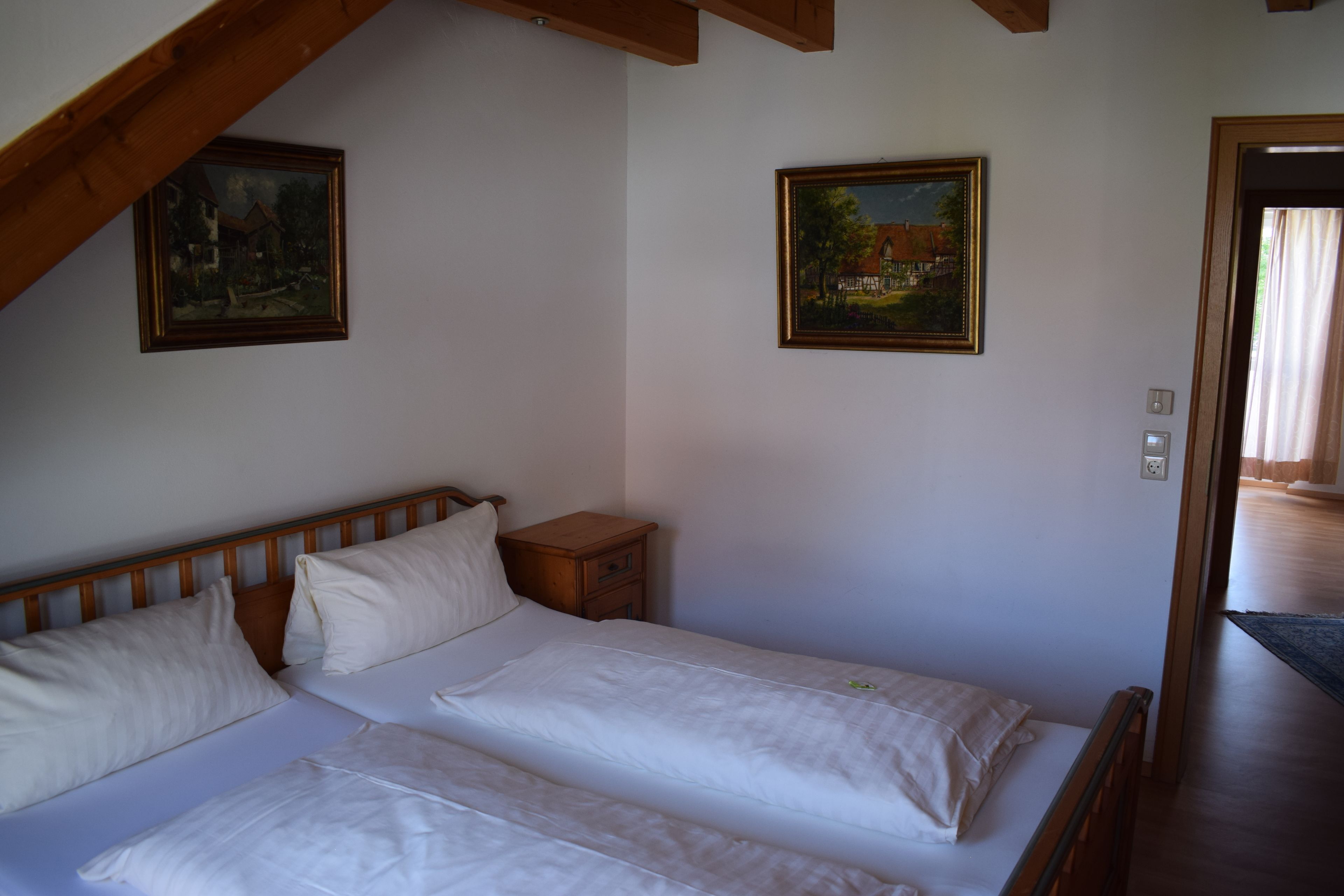 A bedroom with two beds, wooden headboard, a nightstand, and two framed paintings on the walls.
