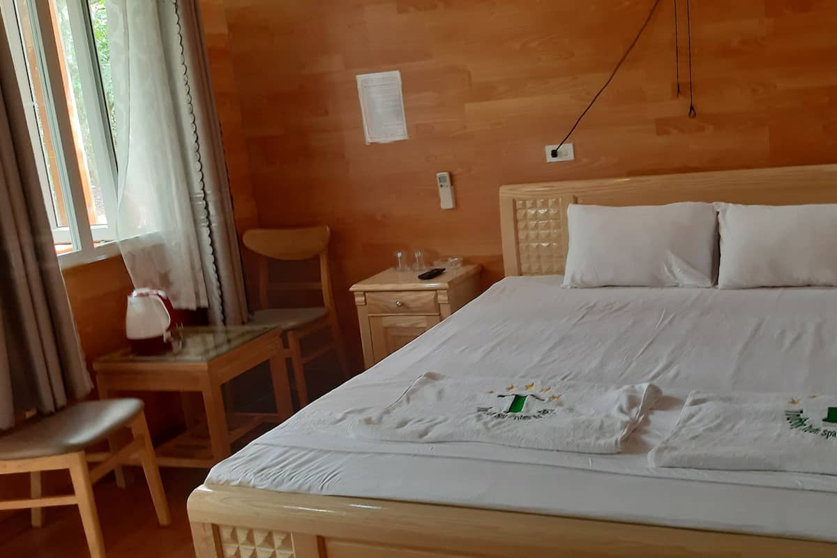 Ett hotellrum med en säng i trä, ett skrivbord med en stol och ett fönster med gardiner.