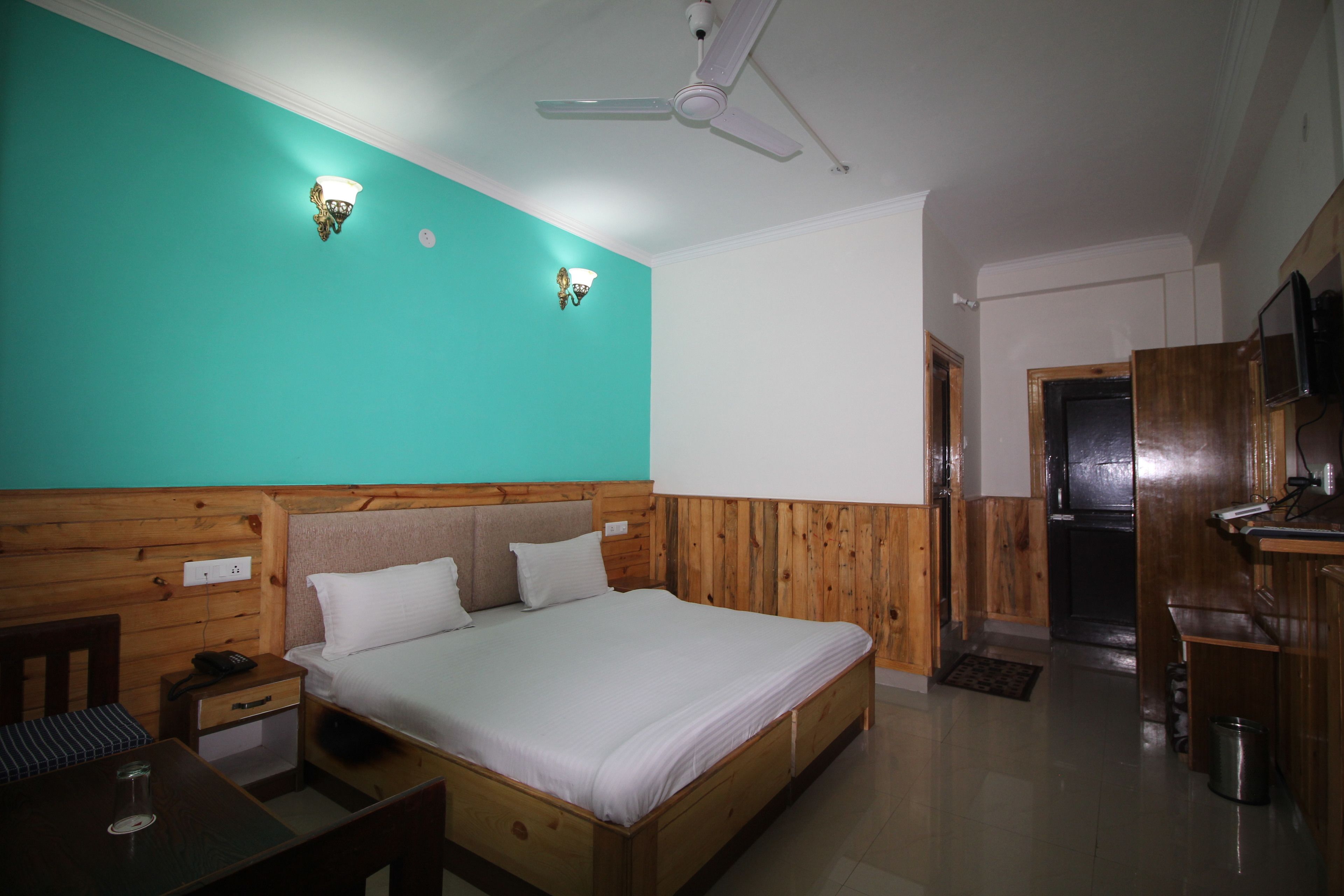 A room with a bed, wooden headboard, teal walls, a ceiling fan, and a small kitchenette.