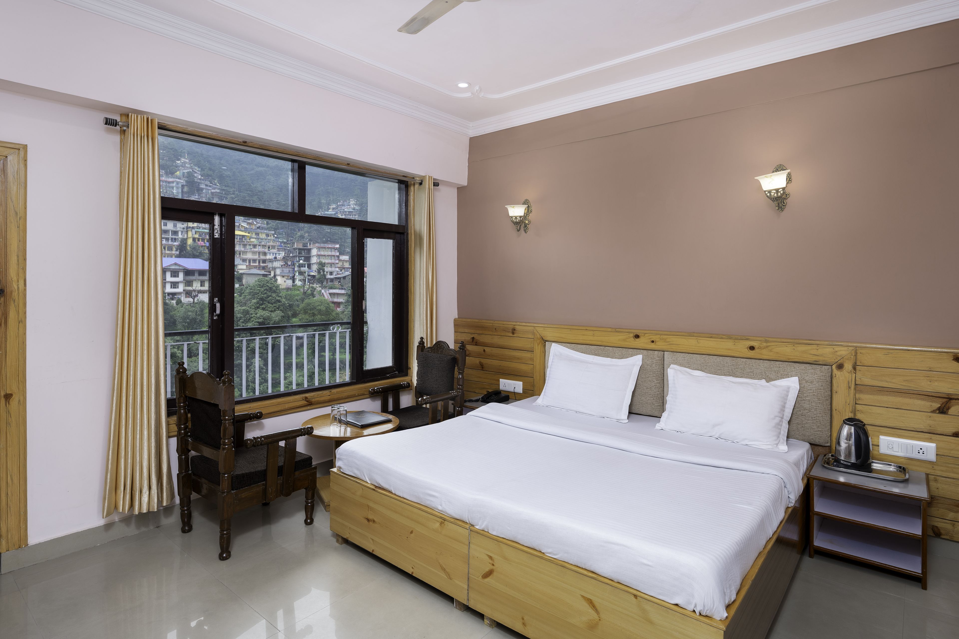 Une chambre d’hôtel avec un lit en bois, un bureau et une chaise, une fenêtre avec des rideaux et deux lampes fixées au mur.