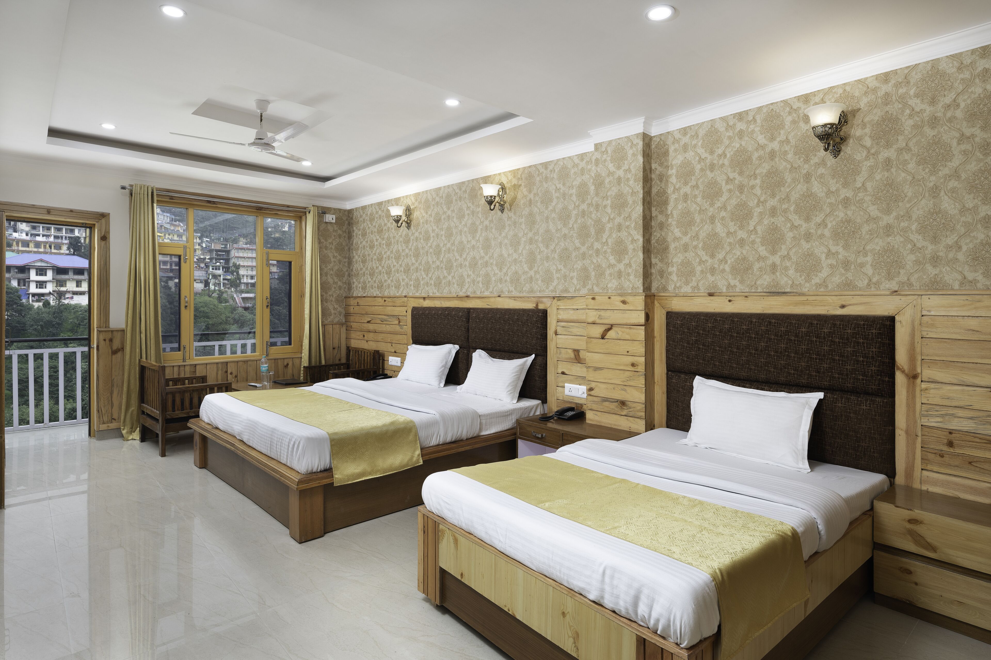 A hotel room with two beds, wooden headboards, a balcony, and a view of the city.