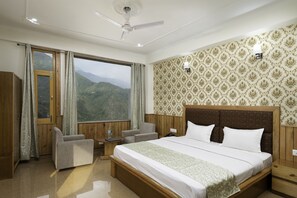 A hotel room with a large bed, a desk, a chair, a small table, and a view of mountains through a large window. - Hotel Mount View (Dharamshala)