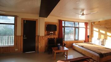 A room with a bed, a table, a television, and a window with curtains.