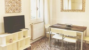 A room with a television on a white shelf, a dining table with chairs, a radiator, and a window with curtains. - Rosso apartment, first floor (Unknown)