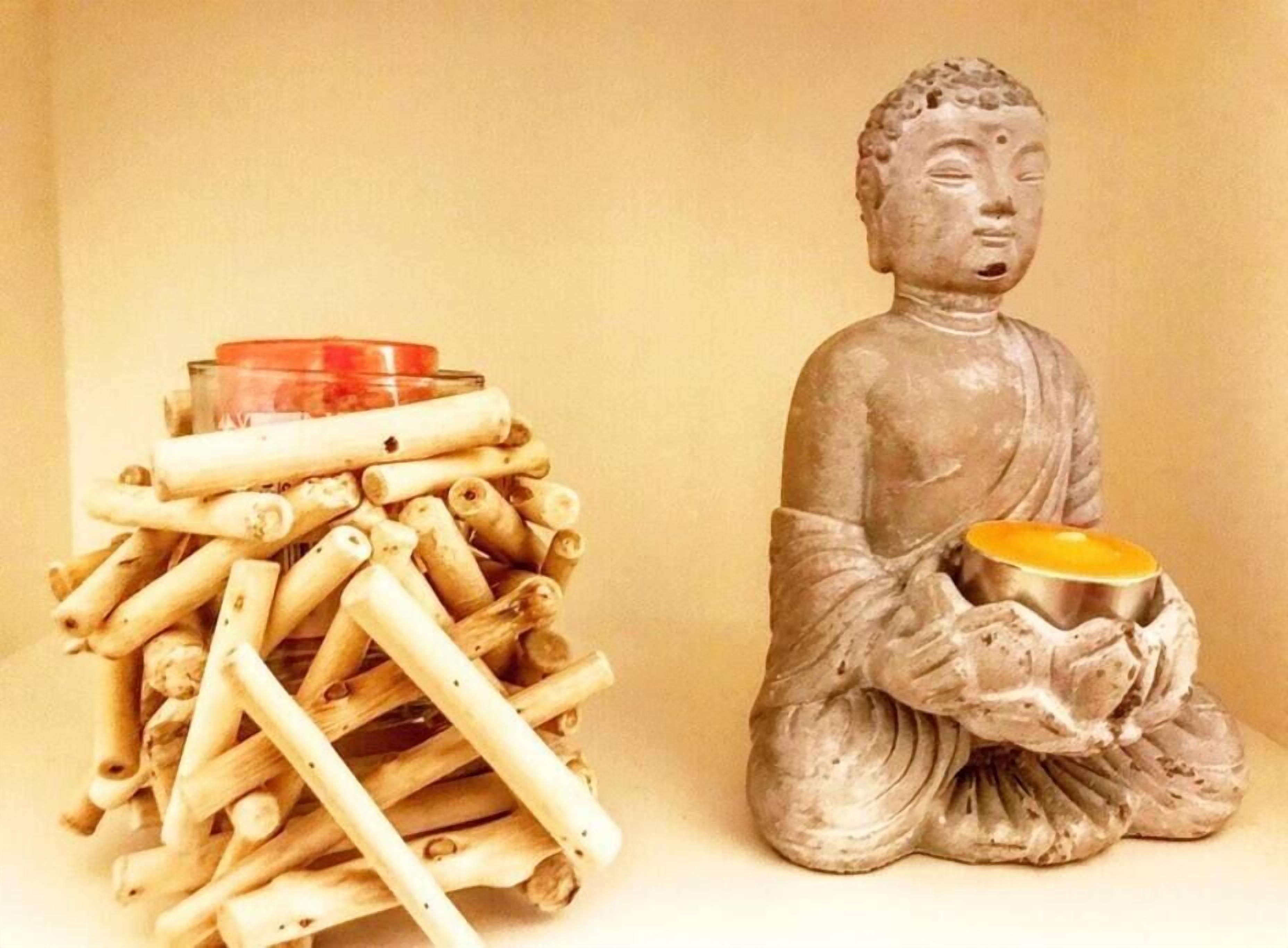 A statue of a seated figure holding a bowl, next to a pile of sticks with a red container on top.