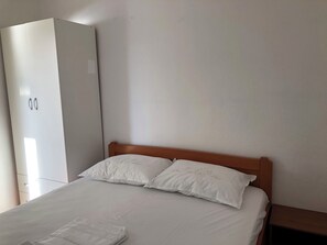 Una camera da letto con un letto, due cuscini, una testiera in legno e un armadio bianco.