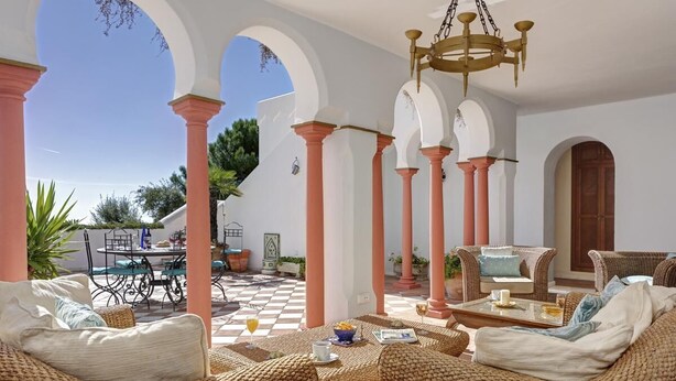 A sunlit outdoor seating area with wicker furniture, a checkered floor, and a view of the surrounding landscape. - Villa with infinity pool (Gaucín)