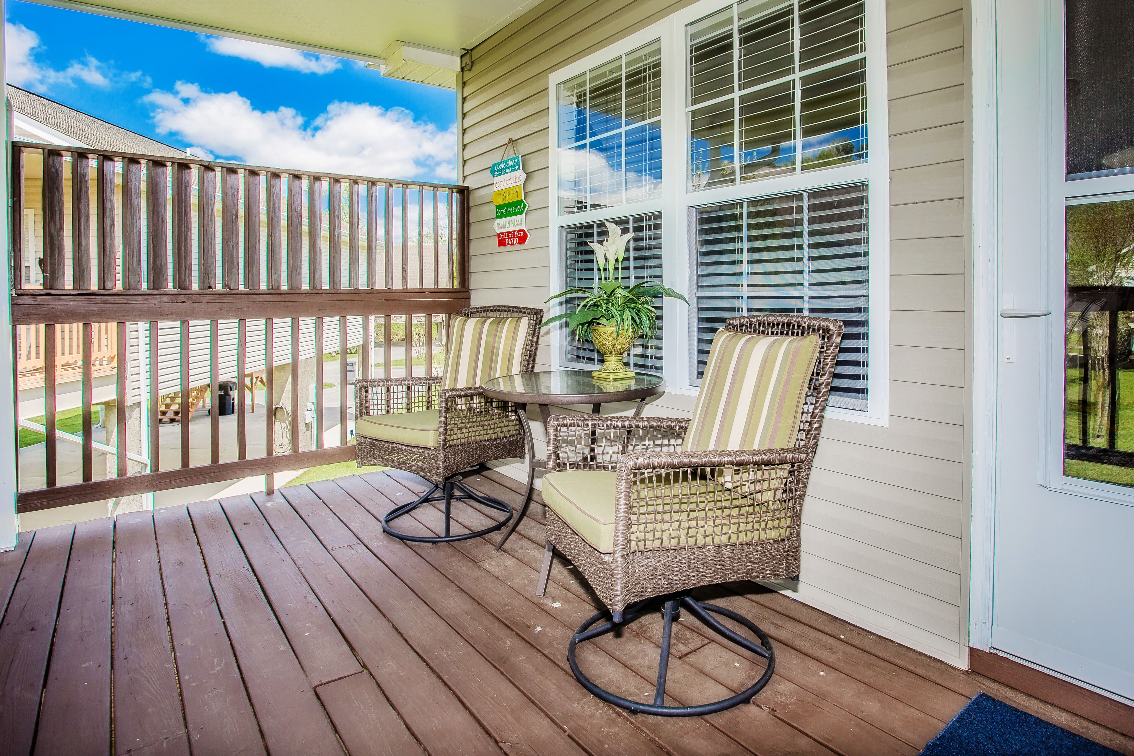 A wooden deck with wicker chairs and a table, a potted plant, and a sign with directional arrows.