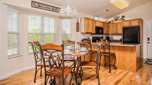 A kitchen with wooden cabinets, a black refrigerator, and a dining area with a wooden table and metal chairs.