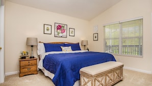 A bedroom with a large bed, two bedside tables, a bench, and a window with blinds.