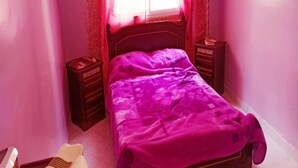 Een slaapkamer met een bed, nachtkastje en een raam met gordijnen.