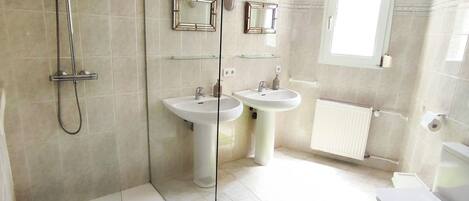 Un baño moderno con ducha de vidrio, dos lavamanos, un inodoro y una ventana.