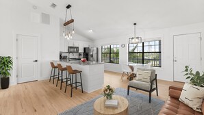 Een ruime woonkamer met een keukeneiland, barstoelen, een ronde salontafel en een leren bank.
