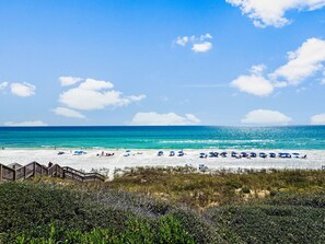 A beach with a wooden boardwalk leading to the shore, clear turquoise waters, and a sandy beach with umbrellas. - Spacious 30A Townhome with Private Beach Access 50ft Away (Panama City Beach)