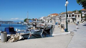 A coastal marina with boats docked, a paved walkway, and historic buildings along the shore. - Elata-apartments (Thasos)