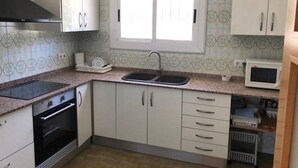 Een keuken met witte kasten, een zwarte kookplaat, een magnetron en een raam boven de gootsteen.