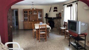Een woonkamer met een open haard, een televisie en een eethoek met houten stoelen en een tafel.