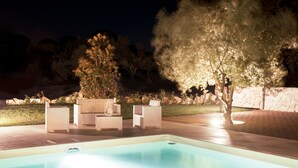 Una piscina con sillones de descanso y un árbol.