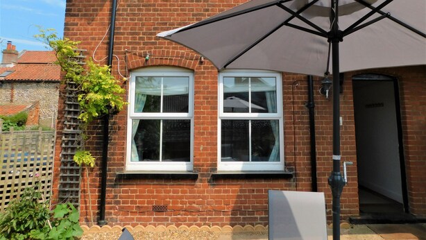 A brick house with two windows, a door, and a large umbrella. - 1 Orchard Cottages -  a cottage that sleeps 5 guests  in 2 bedrooms (Cromer)