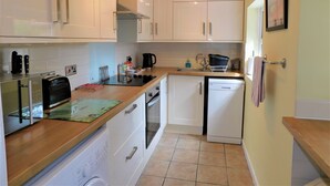 A compact kitchen with white cabinets, a toaster, a kettle, and a dishwasher. - 1 Orchard Cottages -  a cottage that sleeps 5 guests  in 2 bedrooms (Cromer)