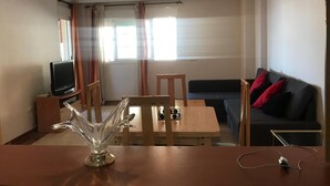 Una sala de estar con televisión, una mesa de comedor, un sofá y un jarrón de cristal decorativo.