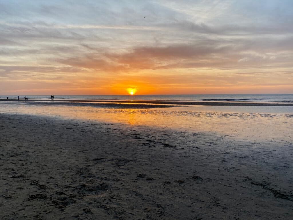 A beach at sunset with a clear sky and calm sea.