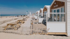 A row of wooden beach huts with a wooden deck and picnic tables, overlooking the beach. - Beach Bungalow Sojo Zandvoort ADULTS ONLY! (Zandvoort)