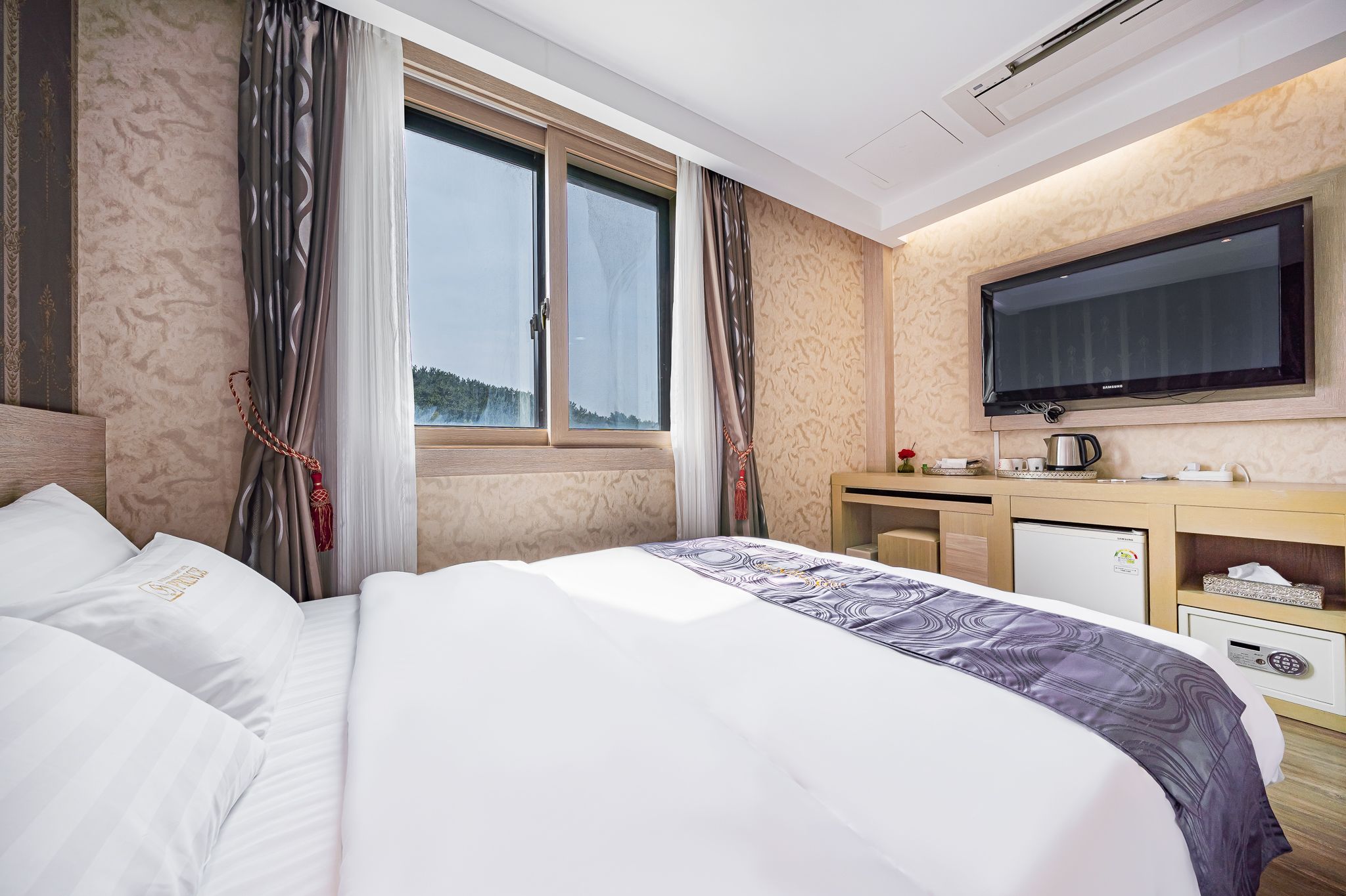 Habitación de hotel con una cama grande, un escritorio con televisor y vistas al exterior a través de la ventana.