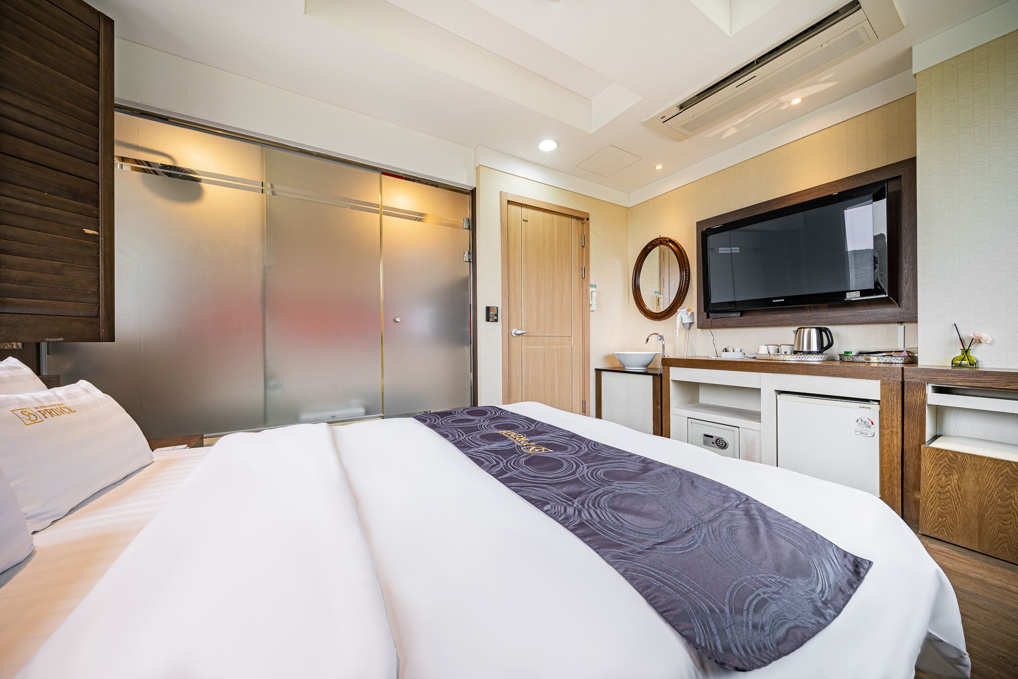 Una habitación de hotel con una cama grande, televisión, una kitchenette pequeña y un armario con puerta corredera.
