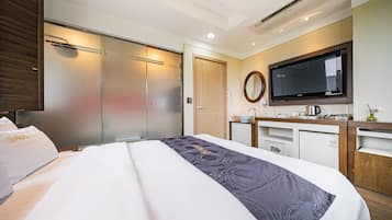 Una habitación de hotel con una cama grande, televisión, una kitchenette pequeña y un armario con puerta corredera.