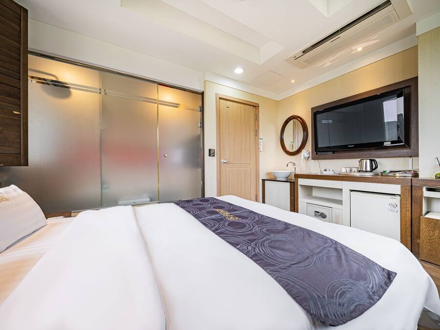 Una habitación de hotel con una cama grande, televisión, una kitchenette pequeña y un armario con puerta corredera.