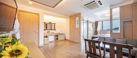 Una habitación de hotel moderna con suelo de madera, una kitchenette, un sofá y un amplio ventanal con vistas.