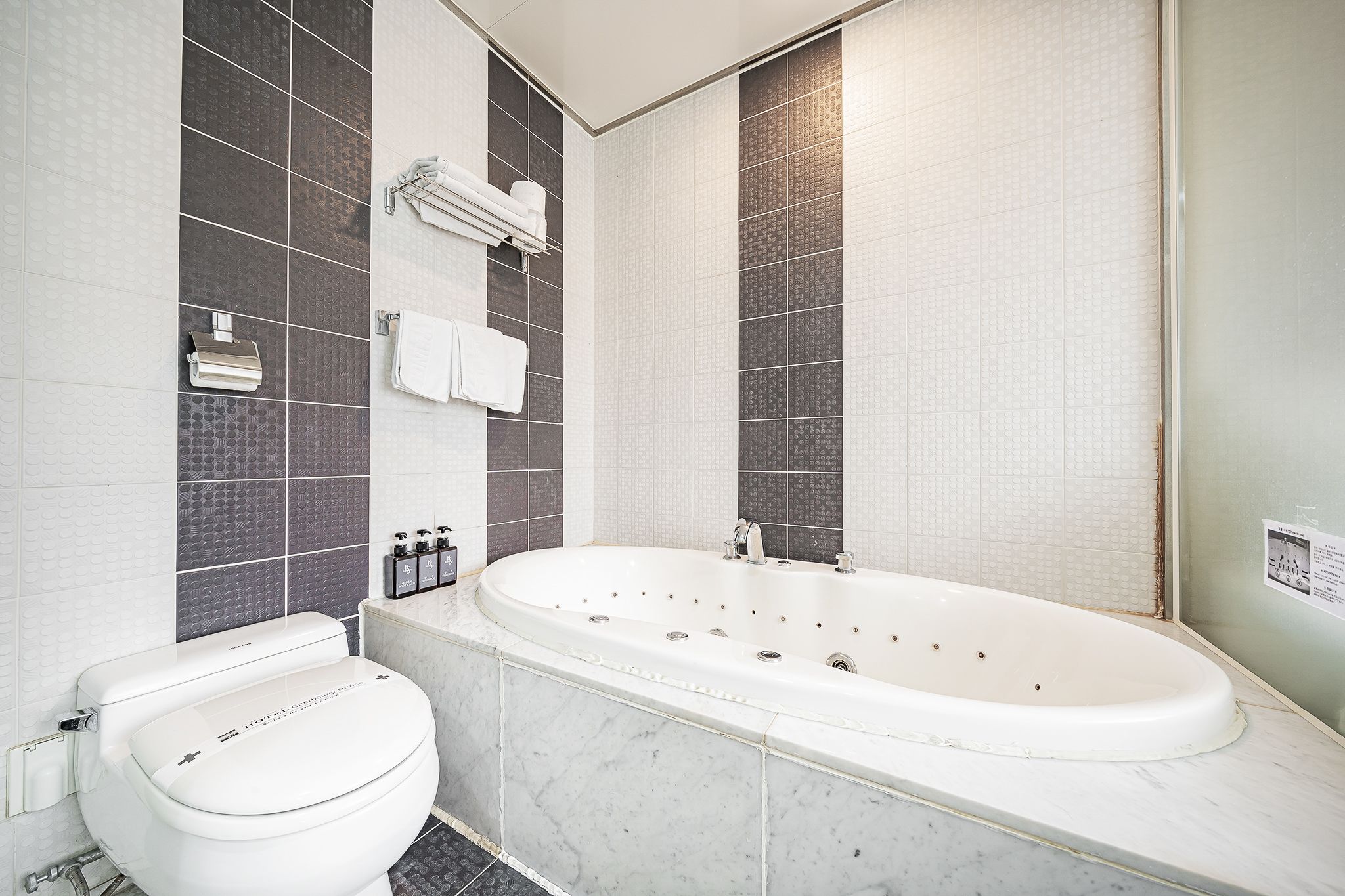 A modern bathroom with a white toilet, a freestanding bathtub, and dark tiled walls.