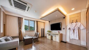 A modern hotel room with a sofa, dining table, chairs, a TV, a desk with a computer, and a wardrobe with robes. - Incheon Prince Tourist Hotel (Incheon)