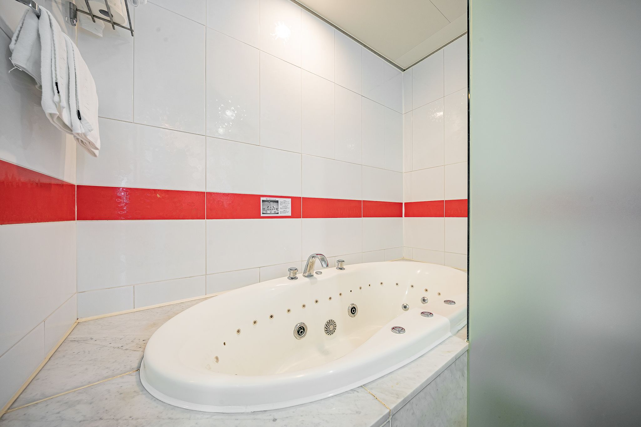 Ein modernes Badezimmer mit einer großen Badewanne, weißen und roten Fliesenwänden und einem sichtbaren Schild an der Wand.