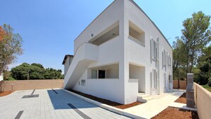 Un bâtiment moderne, de couleur blanche, doté d’un toit en pente, de grandes fenêtres et d’un espace d’entrée pavé.