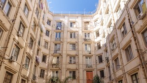 A courtyard with multiple floors of buildings, potted plants, and a clear blue sky. - Bilocale_ Historical Markets (Palermo, Sicilia)