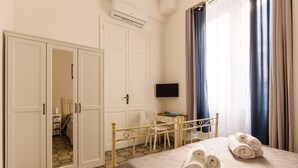 A hotel room with a bed, a wardrobe, a desk, a television, and a window with curtains. - Bilocale_ Historical Markets (Palermo, Sicilia)