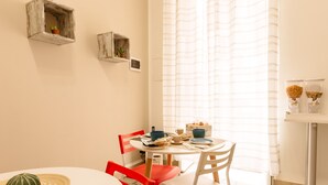 A dining area with a round table, red and white chairs, a small potted plant, and a window with sheer curtains. - Bilocale_ Historical Markets (Palermo, Sicilia)