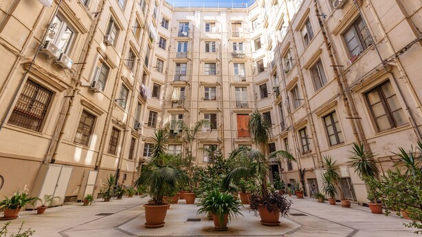 A courtyard with multiple floors of buildings, potted plants, and balconies. - Bilocale_ Historical Markets (Palermo, Sicilia)
