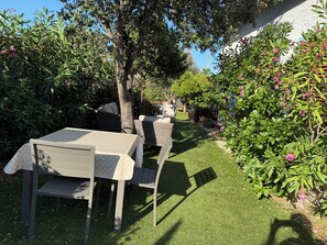 Une terrasse de jardin avec une table et des chaises, entourée d’une végétation luxuriante et de plantes en fleurs.