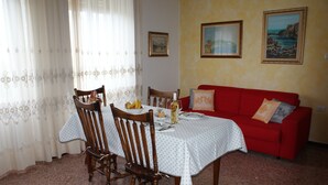 Ein Essbereich mit einem Tisch für zwei Personen, Holzstühle, ein rotes Sofa und zwei gerahmte Bilder an der Wand.