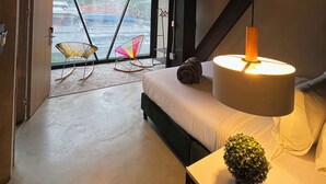 A modern hotel room with a large window, a bed, a hanging lamp, and a small table with a decorative item. - Hotel Lleras Park Concept (Medellín)