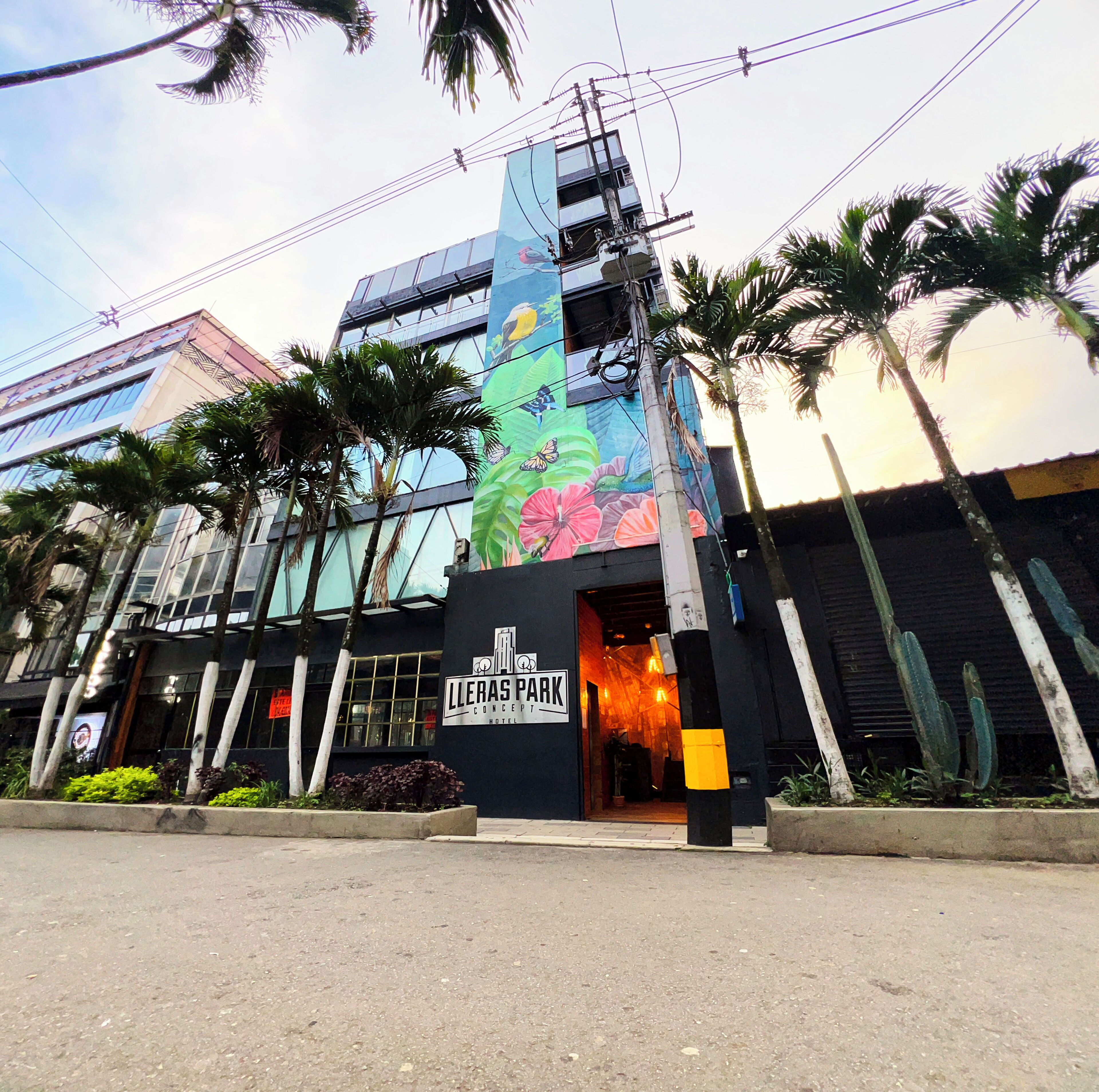 Entrada de un hotel con un mural colorido, palmeras y un cartel que dice 'Lleras Park Concept Hotel'.