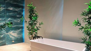 A modern bathroom with a large bathtub, two potted plants, and a marble wall. - Hotel Lleras Park Concept (Medellín)