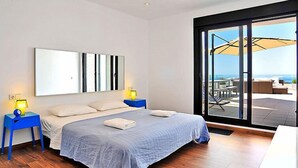 A modern bedroom with a large bed, two bedside tables with lamps, a large window with a view of the sea, and a sliding glass door leading to an outdoor seating area. - Vacation home Megin by Interhome (Moraira)