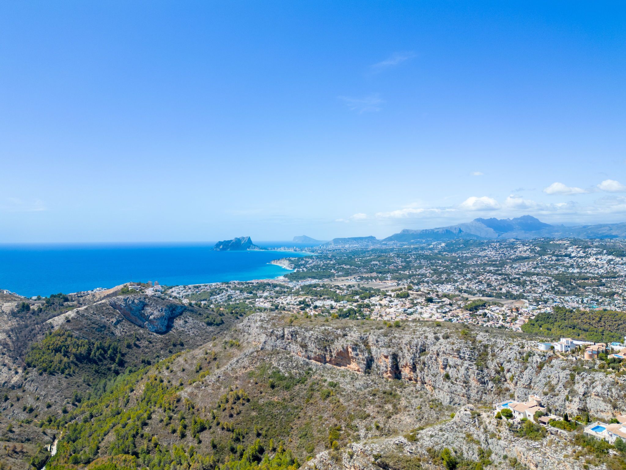 A coastal town with a mountainous backdrop, featuring a mix of residential and commercial buildings, and a prominent rocky outcrop in the foreground.