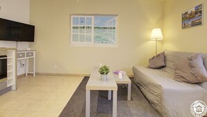 A living room with a TV, a window with a view of water, a sofa, a table with a plant, and a lamp. - Gîte du Héron Gris (BOULIGNEUX)