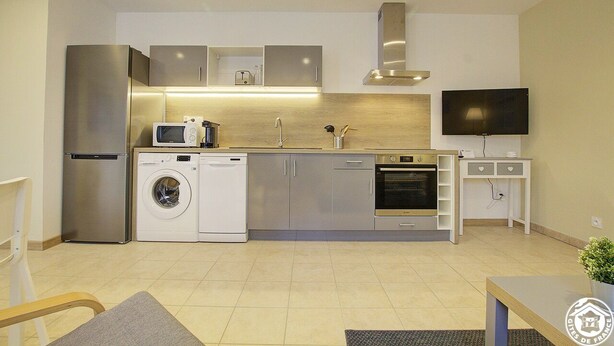 A compact kitchen with a stainless steel refrigerator, a microwave, a washing machine, a dishwasher, and a built-in oven. - Gîte du Héron Gris (BOULIGNEUX)